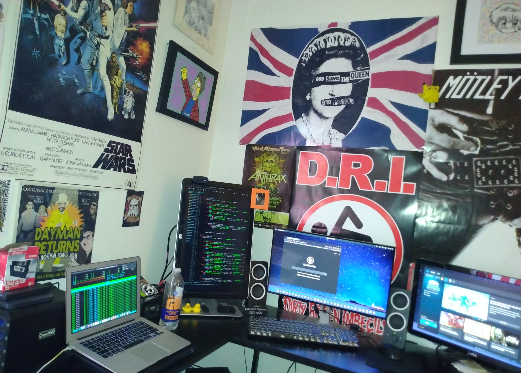 A desk setup with four computer monitors, a keyboard, speakers, two rubber ducks, and many posters on the walls.