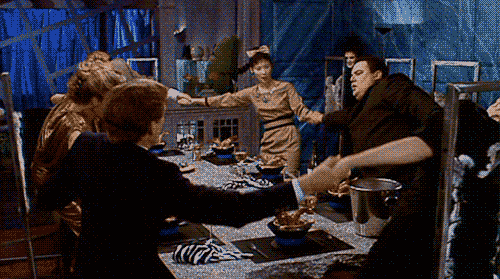 Six people hold hands around a dinner table, flailing from side to side.