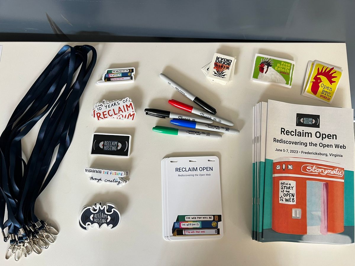 A welcome table with lanyards, Reclaim Hosting and open edtech-themed stickers, nametags, markers, and programs.
